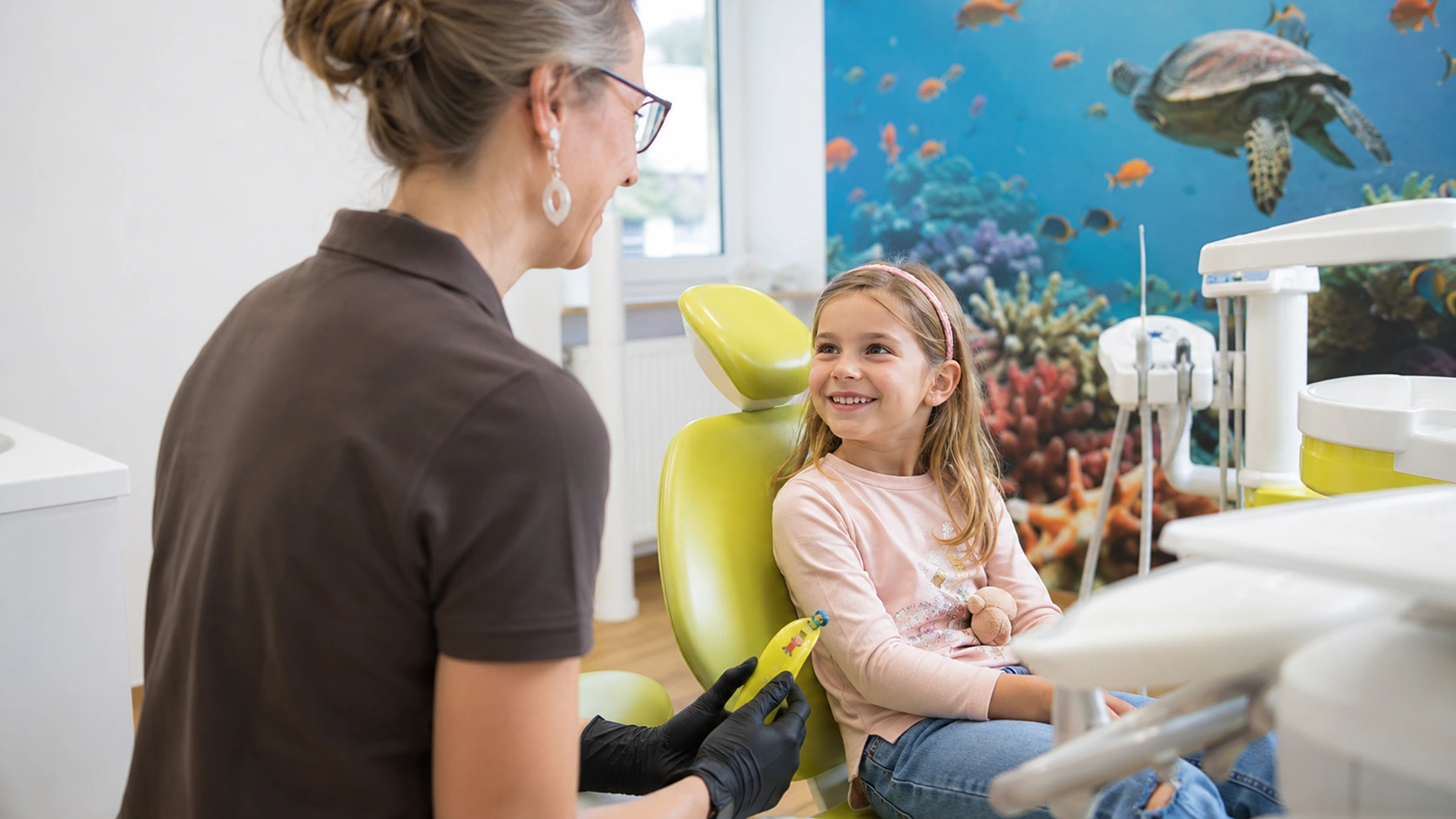 familydentist-zahnarzt-kinder Kinderzahnärztin behandelt ein lächelndes Mädchen im Kinderbereich der Zahnarztpraxis Family Dentist in Marburg